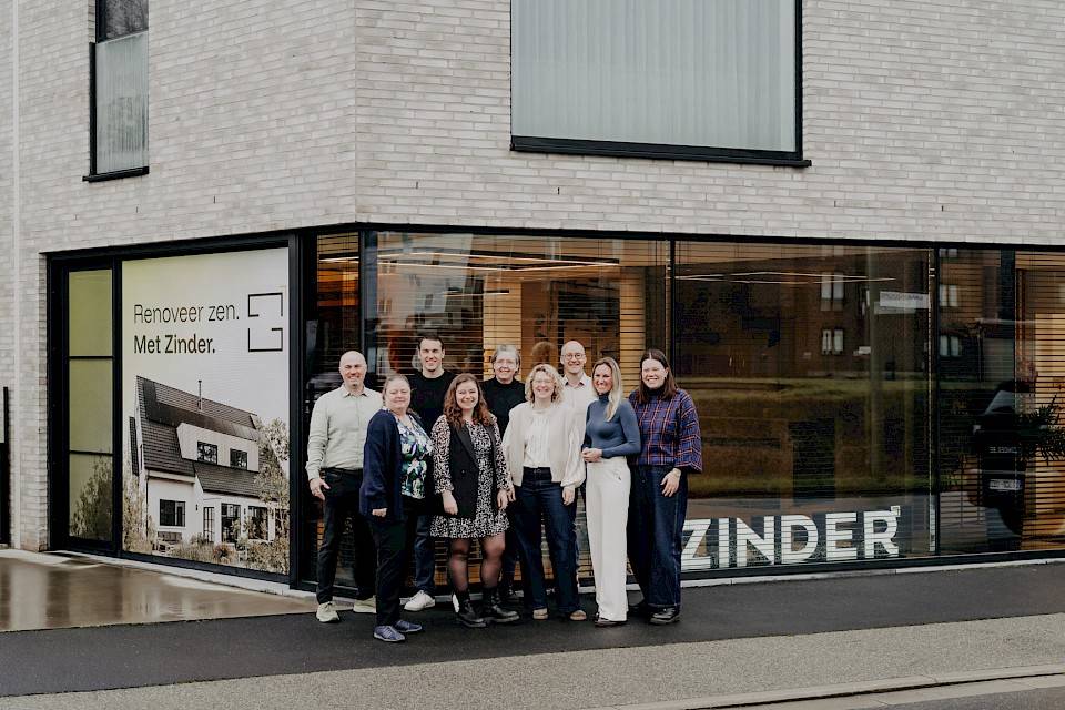 Het team van Zinder dat poseert voor hun bestelwagen met op de achtergrond een huis in opbouw.
